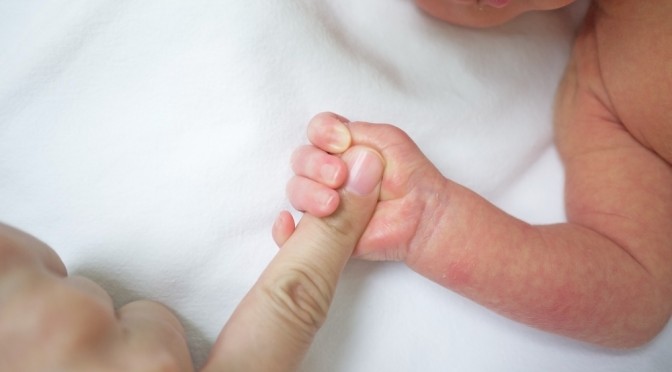 Ръчичка на бебе държи пръст на възрастен